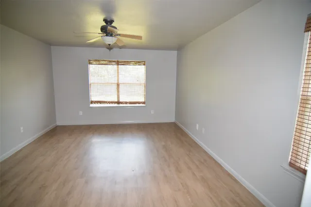 an empty room with wooden floor chandelier fan and windows