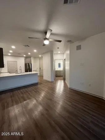a view of an empty room with wooden floor and a kitchen