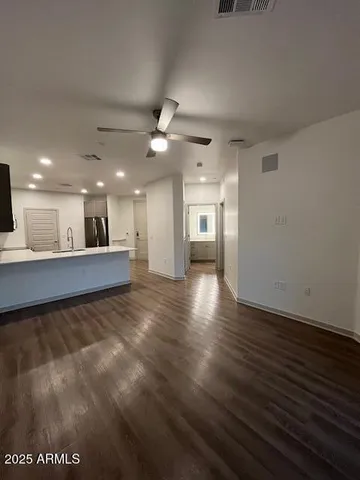 a view of an empty room with wooden floor and a kitchen