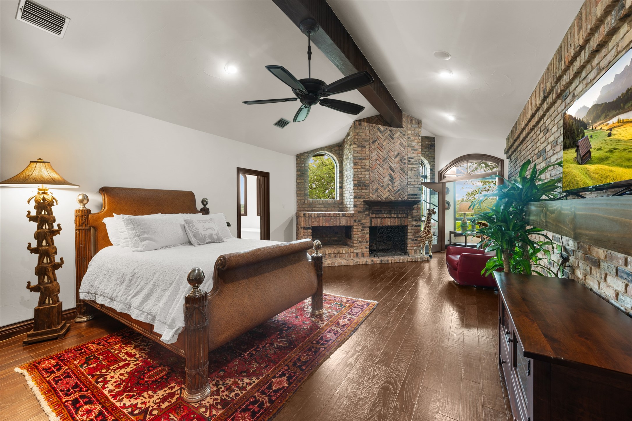 34000 Smithson Valley Road Bulverde, TX 78163 - Photo 17 of 50 The primary suite showcases a stunning double-sided brick fireplace and soaring ceilings, blending rustic elegance with timeless design. Large windows frame beautiful views while filling the space with natural light.