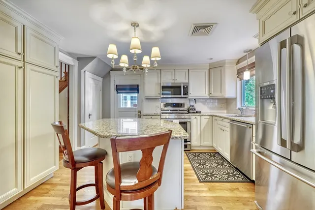 a kitchen with stainless steel appliances kitchen island granite countertop a refrigerator a stove a sink dishwasher and white cabinets with wooden floor