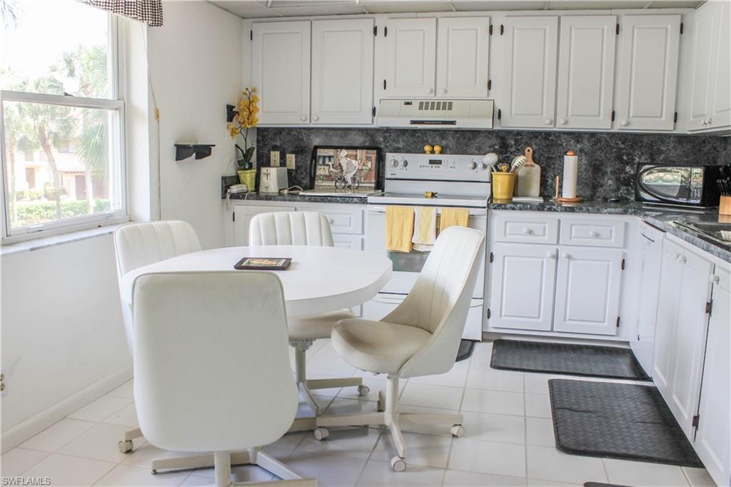 197 Albi Road, Unit 202 Naples, FL 34112 - Photo 4 of 12 a kitchen with a white cabinets and chairs