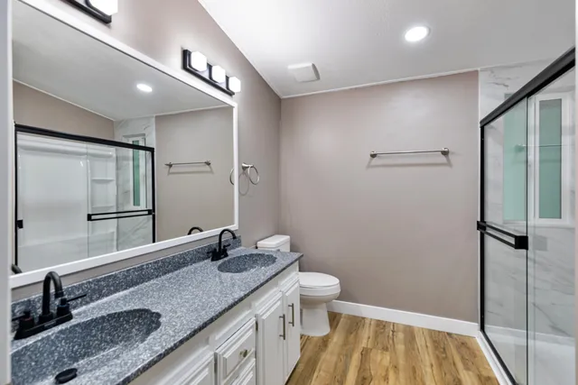 a bathroom with a granite countertop sink a toilet a mirror and shower