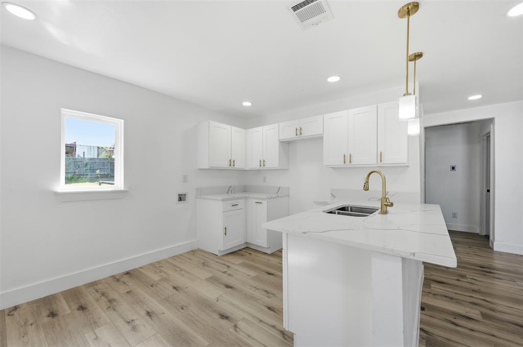 1909 Burchill Road Fort Worth, TX 76105 - Photo 8 of 18 Kitchen featuring an island with a built-in sink, white cabinetry with gold-toned hardware, light-toned countertops, wood-finish flooring, and recessed lighting