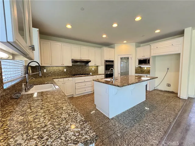 a large kitchen with kitchen island granite countertop a stove a sink a refrigerator a microwave and cabinets