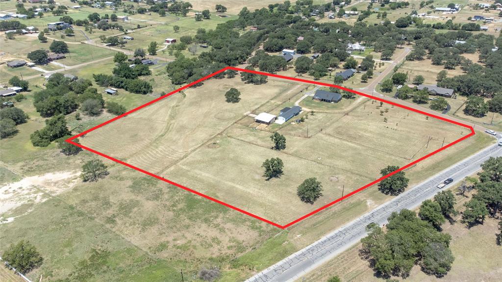 151 County Road 3699 Springtown, TX 76082 - Photo 34 of 35 Expansive property featuring a single-story residence with a dark roof and a detached outbuilding, surrounded by open fields and scattered mature trees