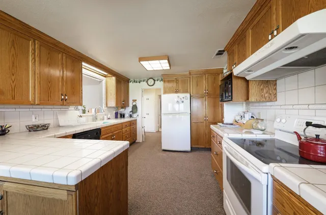 a kitchen with stainless steel appliances granite countertop a sink a stove a refrigerator cabinets and a dining table