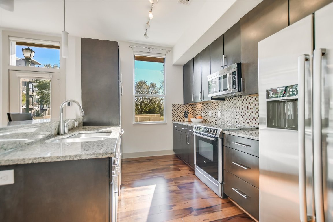 a kitchen with stainless steel appliances granite countertop a refrigerator a stove and a sink