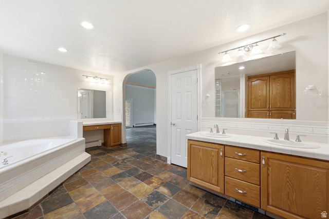 3535 Homestead Road Park City, UT 84098 - Photo 40 of 81 Spacious bathroom featuring a dual vanity with oak cabinetry and white countertops, a large jetted tub with tile surround, and an arched doorway leading to an additional space