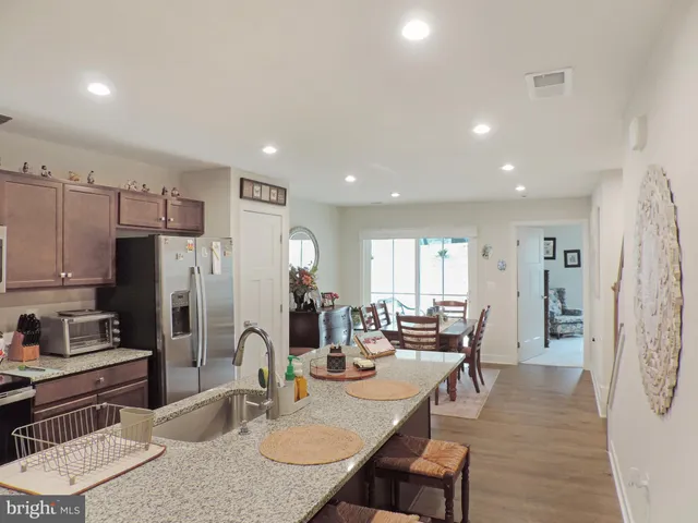 a kitchen with stainless steel appliances granite countertop a refrigerator a stove a sink a dining table and chairs with wooden floor