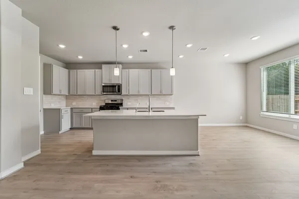 a large kitchen with stainless steel appliances granite countertop a stove a sink a refrigerator and white cabinets with wooden floor