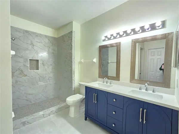 a bathroom with double vanity sink a toilet a mirror and shower