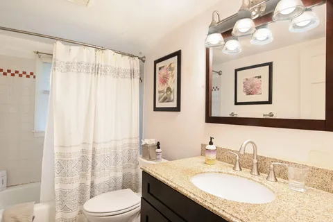 a bathroom with a granite countertop sink a toilet a mirror a vanity a lamp and shower