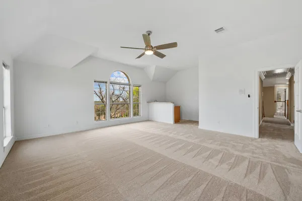 an empty room with chandelier fan and windows