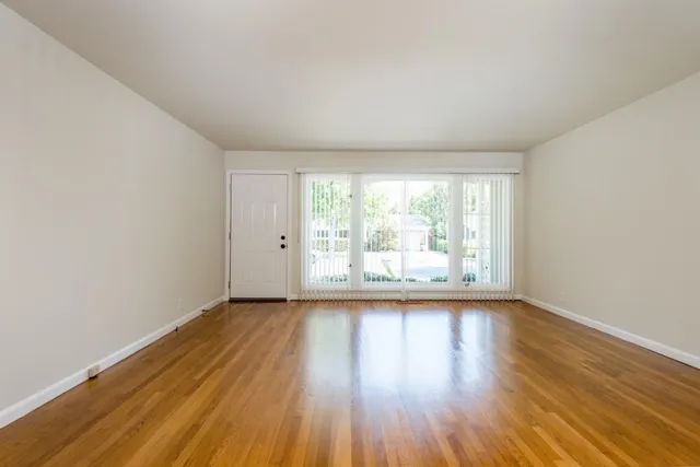 a view of an empty room with wooden floor and a window
