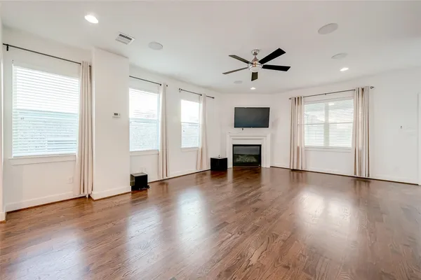 an empty room with wooden floor a ceiling fan windows and a ceiling fan