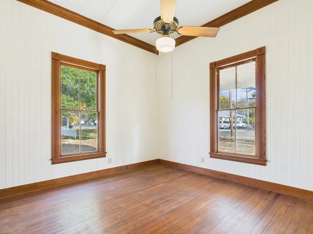 an empty room with wooden floor chandelier fan and windows