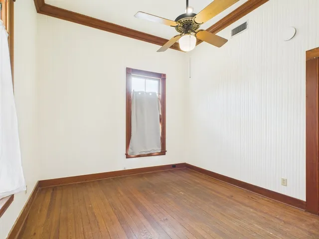 an empty room with wooden floor fan and windows