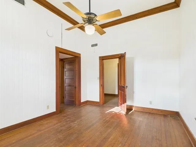 an empty room with wooden floor fan and windows