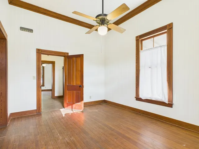 an empty room with wooden floor and a ceiling fan