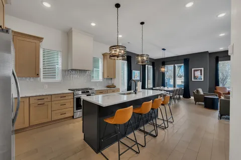 a kitchen with granite countertop a stove a sink a dining table and chairs with wooden floor