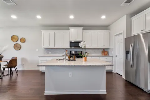 a kitchen with stainless steel appliances granite countertop a sink dishwasher a refrigerator and white cabinets with wooden floor