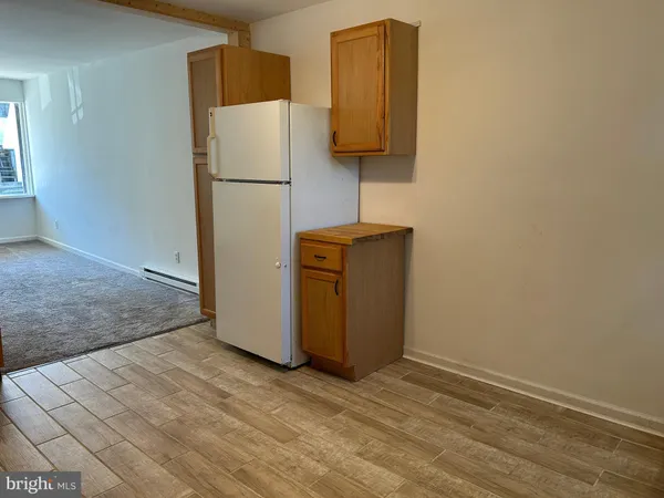 a view of a refrigerator in kitchen and an empty room with wooden floor