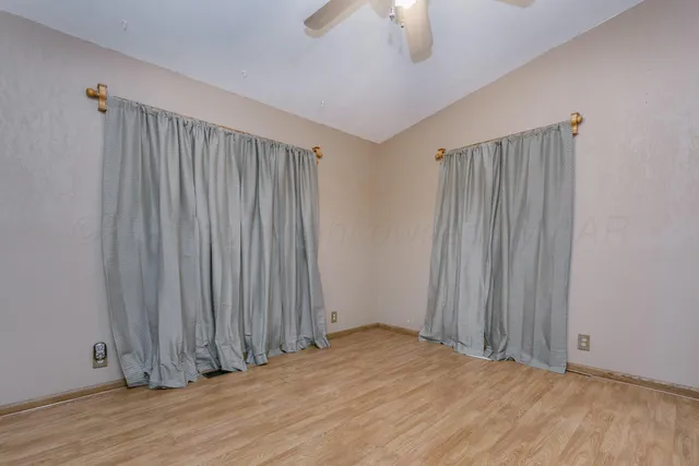 an empty room with wooden floor chandelier fan and windows
