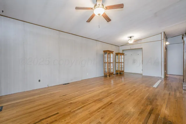 a view of empty room with wooden floor and fan