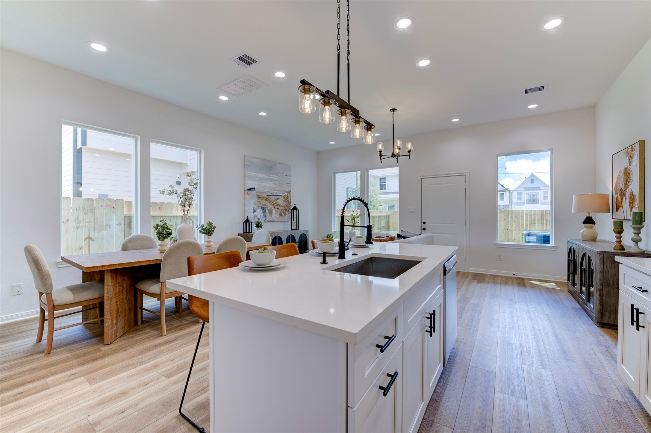 6807 Paris Street Houston, TX 77021 - Photo 21 of 50 Wide view from kitchen island showing open flow to dining table, multiple large windows on three sides, matte black pendant lighting, hardwood floors, and rear exit door.