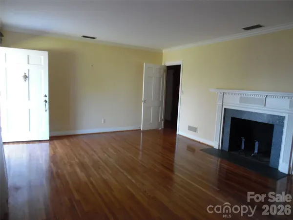 a view of an empty room with wooden floor and a fireplace