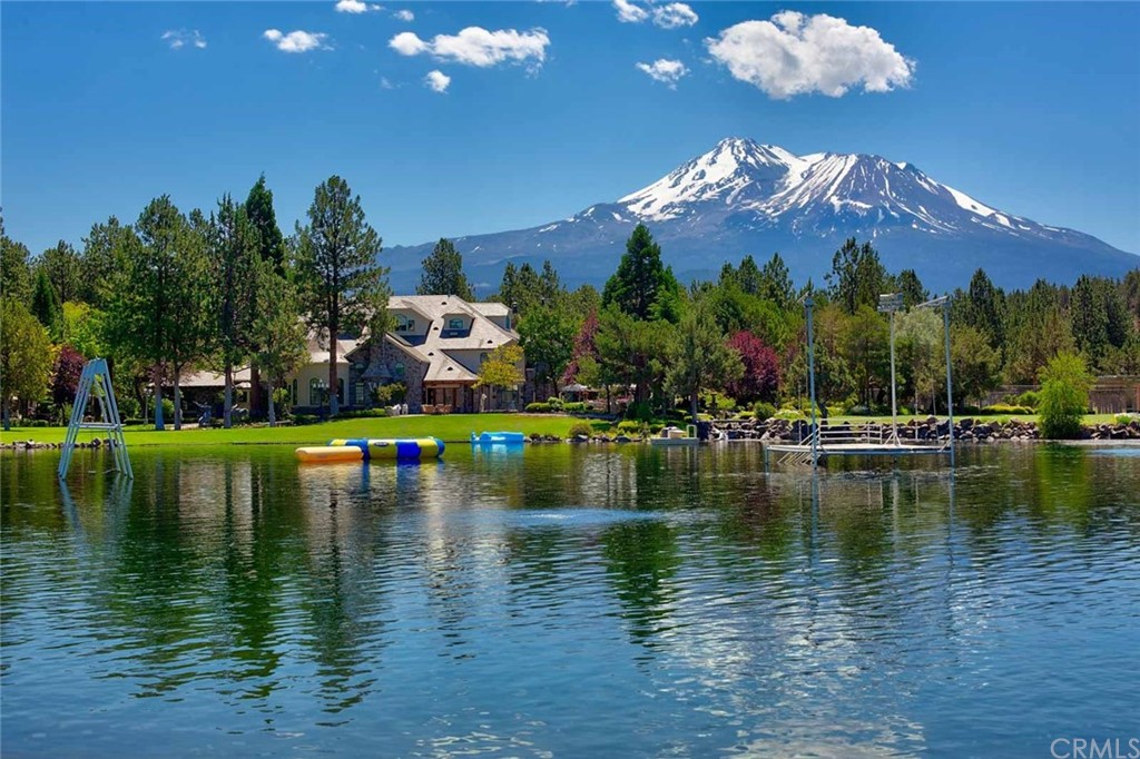a view of a lake in front of house with a yard and swimming pool