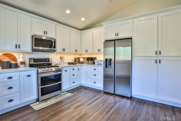 a kitchen with stainless steel appliances granite countertop a refrigerator oven a sink dishwasher and white cabinets with wooden floor