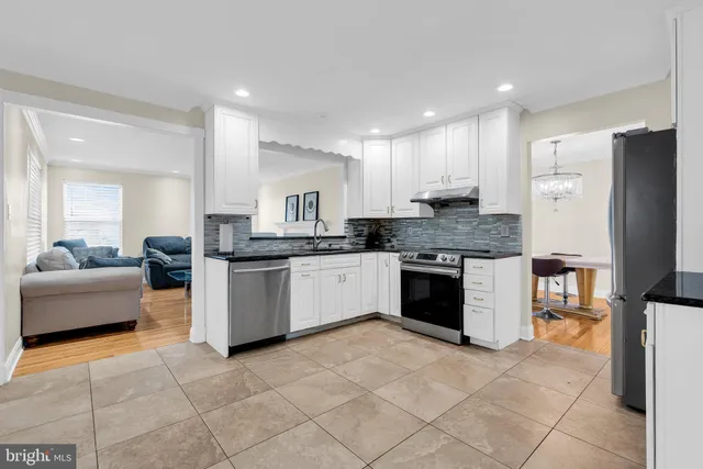 a kitchen with stainless steel appliances granite countertop a stove a sink dishwasher a refrigerator and white cabinets with wooden floor