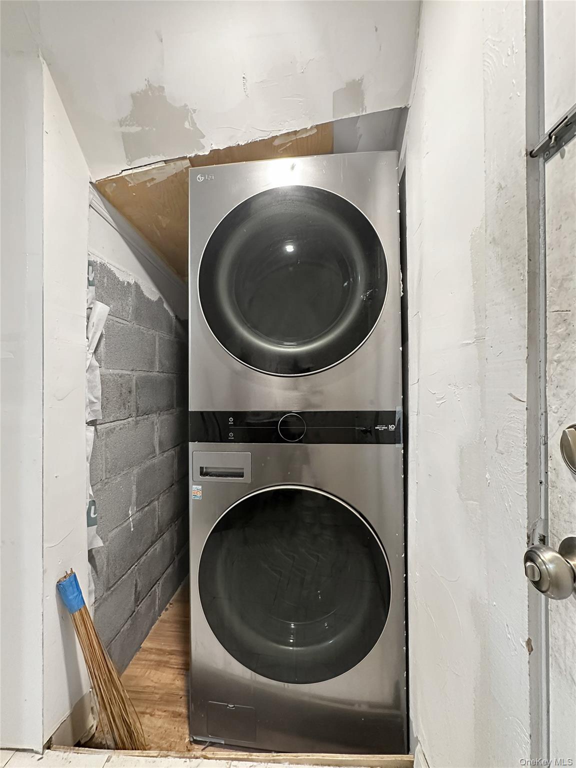 109-66 153rd Street Queens, NY 11433 - Photo 4 of 15 Laundry area with stacked washing machine and dryer, concrete block wall, and wood finished floors