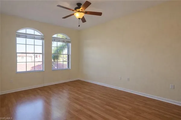 an empty room with wooden floor fan and windows