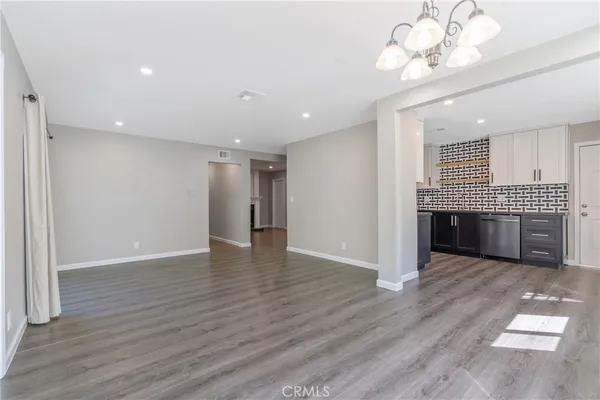 a view of a livingroom with a chandelier wooden floor and a kitchen