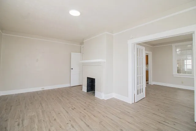 an empty room with wooden floor fireplace and windows
