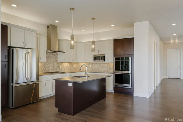 a kitchen with stainless steel appliances granite countertop a refrigerator a sink a stove and white cabinets with wooden floor