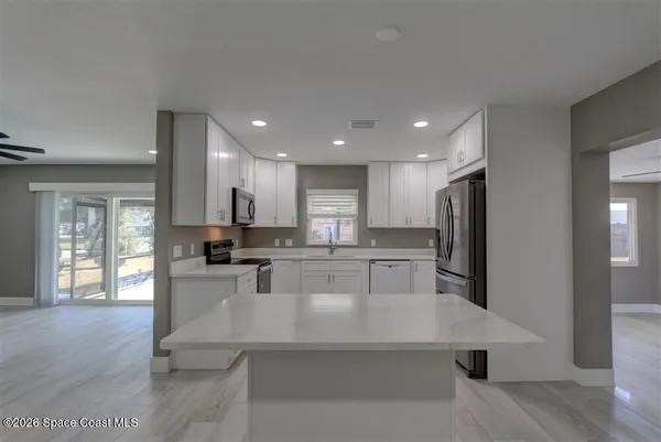 a kitchen with stainless steel appliances kitchen island granite countertop a refrigerator a stove and white cabinets with wooden floor