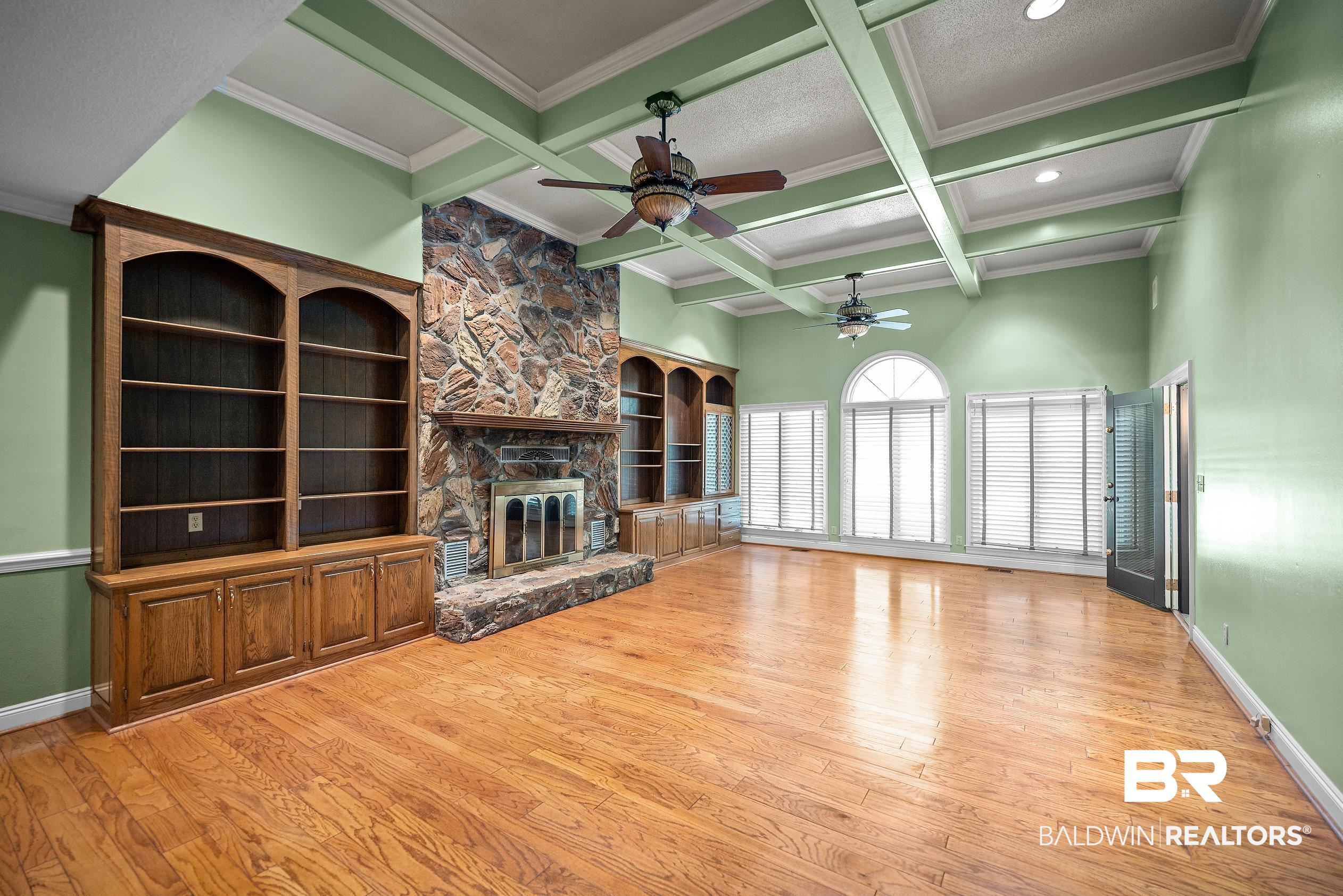 329 Norwood Road Monroeville, AL 36460 - Photo 5 of 49 Spacious room featuring wood-finish flooring, a stone fireplace with built-in cabinetry, coffered ceilings, and multiple windows with blinds