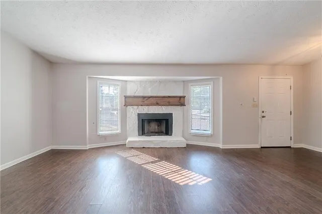 a view of an empty room with wooden floor fireplace and a window