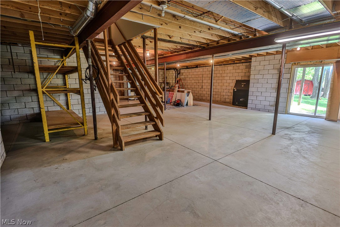 11154 Johnsford Road Southwest Beach City, OH 44608 - Photo 49 of 50 Spacious unfinished basement featuring concrete flooring, exposed ceiling joists, wood stairs, a sliding glass door for exterior access, and concrete block walls