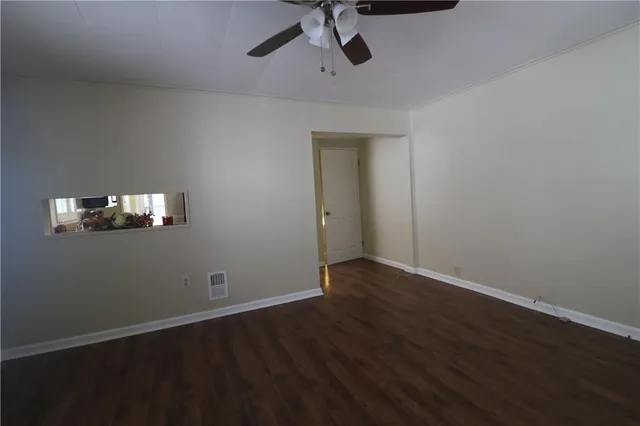 a view of an empty room with wooden floor and a ceiling fan