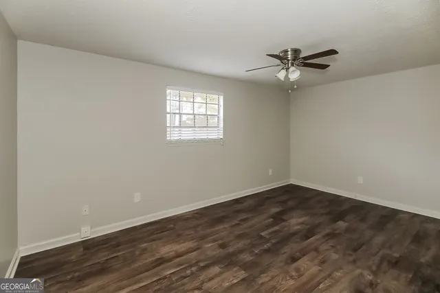 an empty room with wooden floor fan and windows