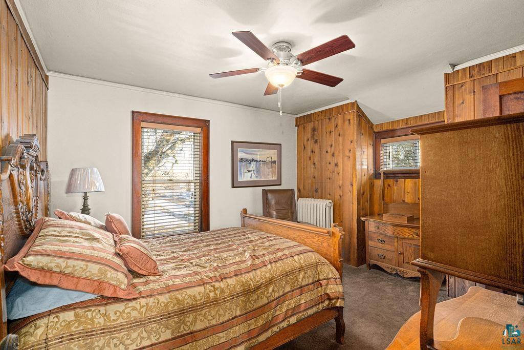 1505 North 19th Street Superior, WI 54880 - Photo 14 of 18 Bedroom with wood walls, radiator heating unit, multiple windows, a ceiling fan, and dark carpet