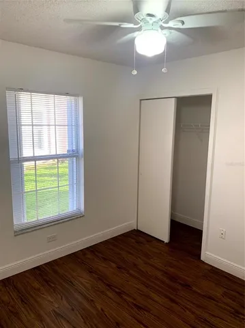 an empty room with wooden floor chandelier fan and windows