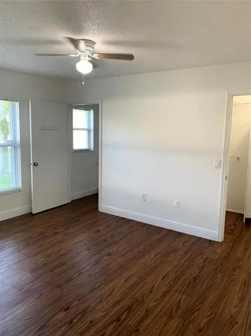 an empty room with wooden floor chandelier fan and windows