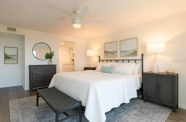 a spacious bedroom with a bed a dresser and potted plants with wooden floor