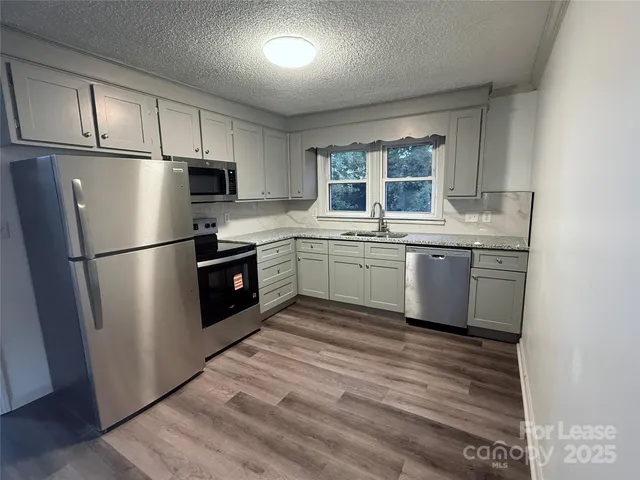 a kitchen with stainless steel appliances granite countertop a refrigerator a sink a stove a refrigerator and white cabinets